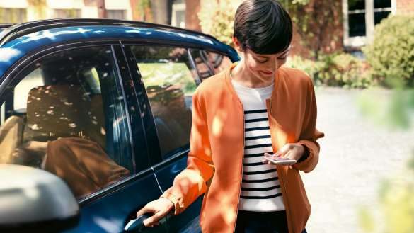 BMW Teleservices Frau guckt auf ihr Smartphone und öffnet Tür ihres BMW